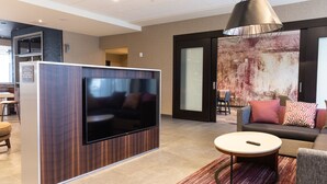 A modern lobby with a large flat-screen TV mounted on a wooden panel, a round coffee table, and a sofa with patterned cushions. - Courtyard by Marriott Cartersville (Cartersville)