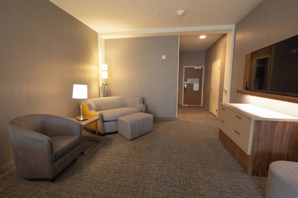 Une chambre d’hôtel avec un canapé, une petite table avec une lampe, un bureau avec des tiroirs et un grand miroir au mur.