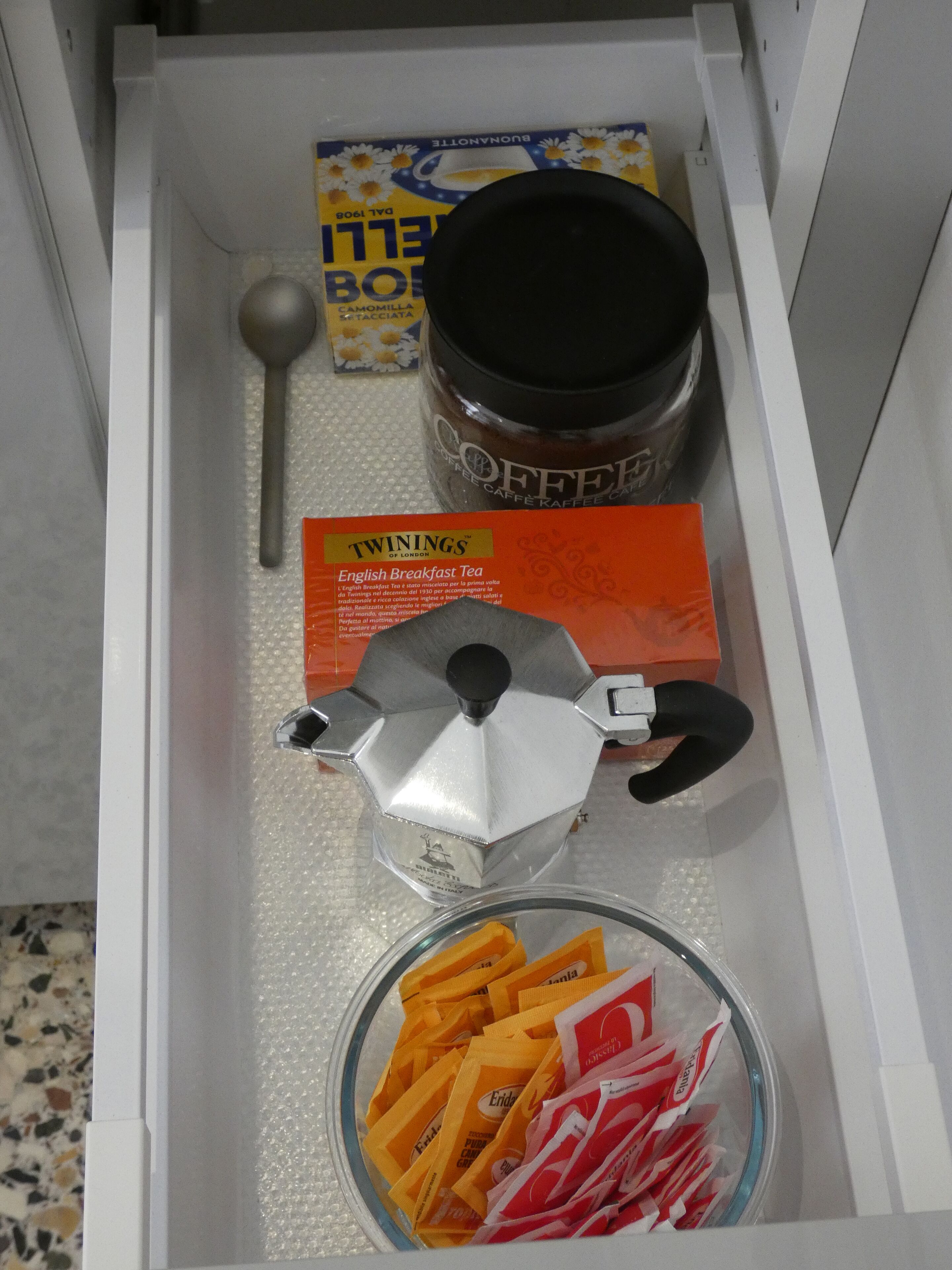 A drawer containing a coffee maker, tea bags, a spoon, and a box of Twinings English Breakfast Tea.