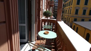 Un balcón con una pequeña mesa y sillas, una planta en maceta y vistas a edificios cercanos.