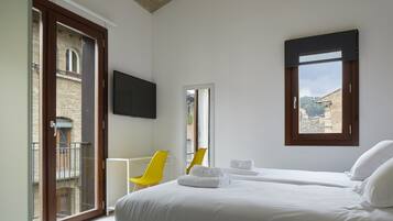 Habitació d'hotel amb llit, televisió, balcó amb una cadira i vistes a edificis.