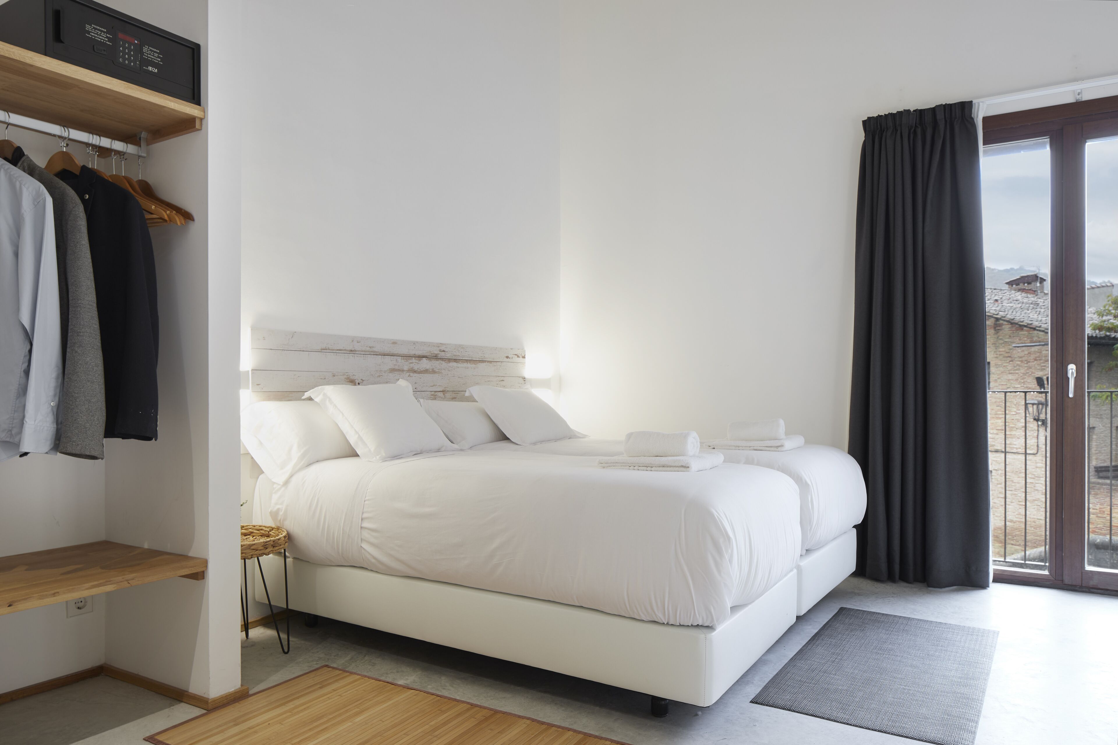 Habitación de hotel con cama, repisa de madera, ventana con cortinas y vistas a edificios.