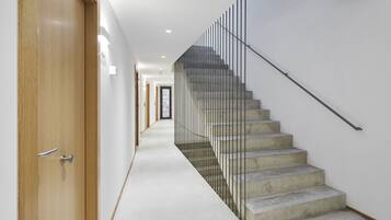 Un interior moderno con una puerta de madera, una escalera de concreto con barandillas metálicas y un pasillo blanco.
