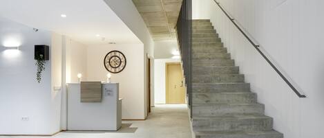 A modern interior with a concrete staircase, a reception desk, and a wall-mounted clock.