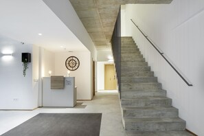 A modern interior with a concrete staircase, a reception desk, and a wall-mounted clock.