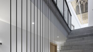 A modern staircase with a metal railing, leading to a high ceiling with skylights.