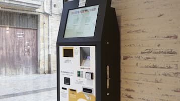 A check-in kiosk with a digital screen, located near a window with a view of a building outside.