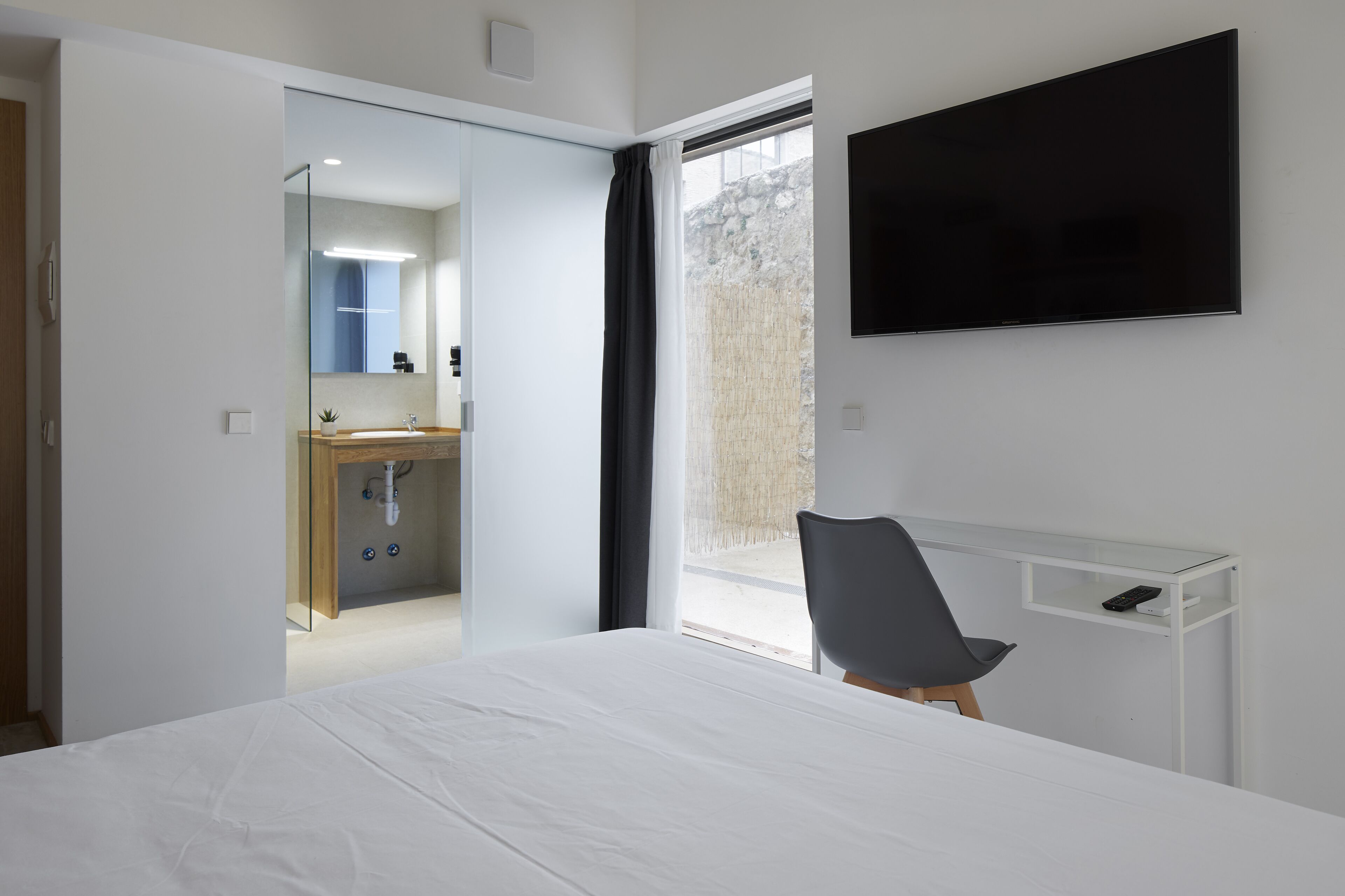 A hotel room with a bed, a desk with a chair, a TV, and a bathroom with a mirror and sink.