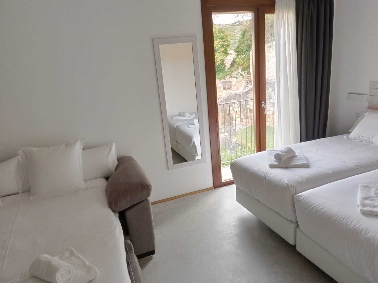 A hotel room with two beds, a large mirror, and a balcony with a view of greenery.