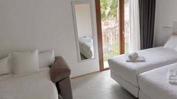 A hotel room with two beds, a large mirror, and a balcony with a view of greenery.