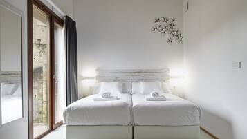 A double bed with white linens and towels, a wooden headboard, and a wall-mounted light fixture.