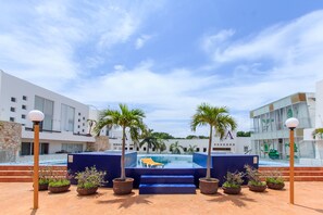 A pool area with a sun lounger, palm trees, and a modern building with a glass facade. - Plaza Paraiso (Playa del Carmen)