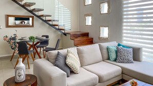 Ein modernes Wohnzimmer mit Treppe, Essbereich und einer Couch mit Zierkissen.