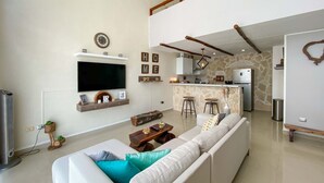 Ein modernes Wohnzimmer mit einer großen Couch, einem Flachbildfernseher und einer Küchenzeile mit Steinwand und Barhocker.
