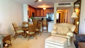 Una sala de estar con un sillón color beige, un pequeño reposapiés y un comedor con sillas de mimbre y una mesa.