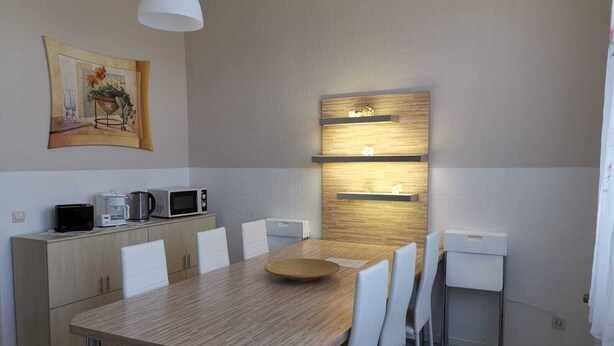A modern dining area with a wooden table, white chairs, a microwave, a coffee maker, and a painting on the wall. - Ferienwohnung Felicity 85 m2 (Solingen)