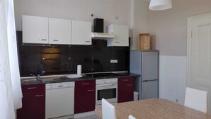 A compact kitchen with white and maroon cabinets, a black backsplash, a white stove, and a small refrigerator. - Ferienwohnung Felicity 85 m2 (Solingen)
