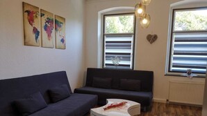 A modern living room with a dark blue sofa, a white coffee table, and a large window with blinds. - Ferienwohnung Felicity 85 m2 (Solingen)