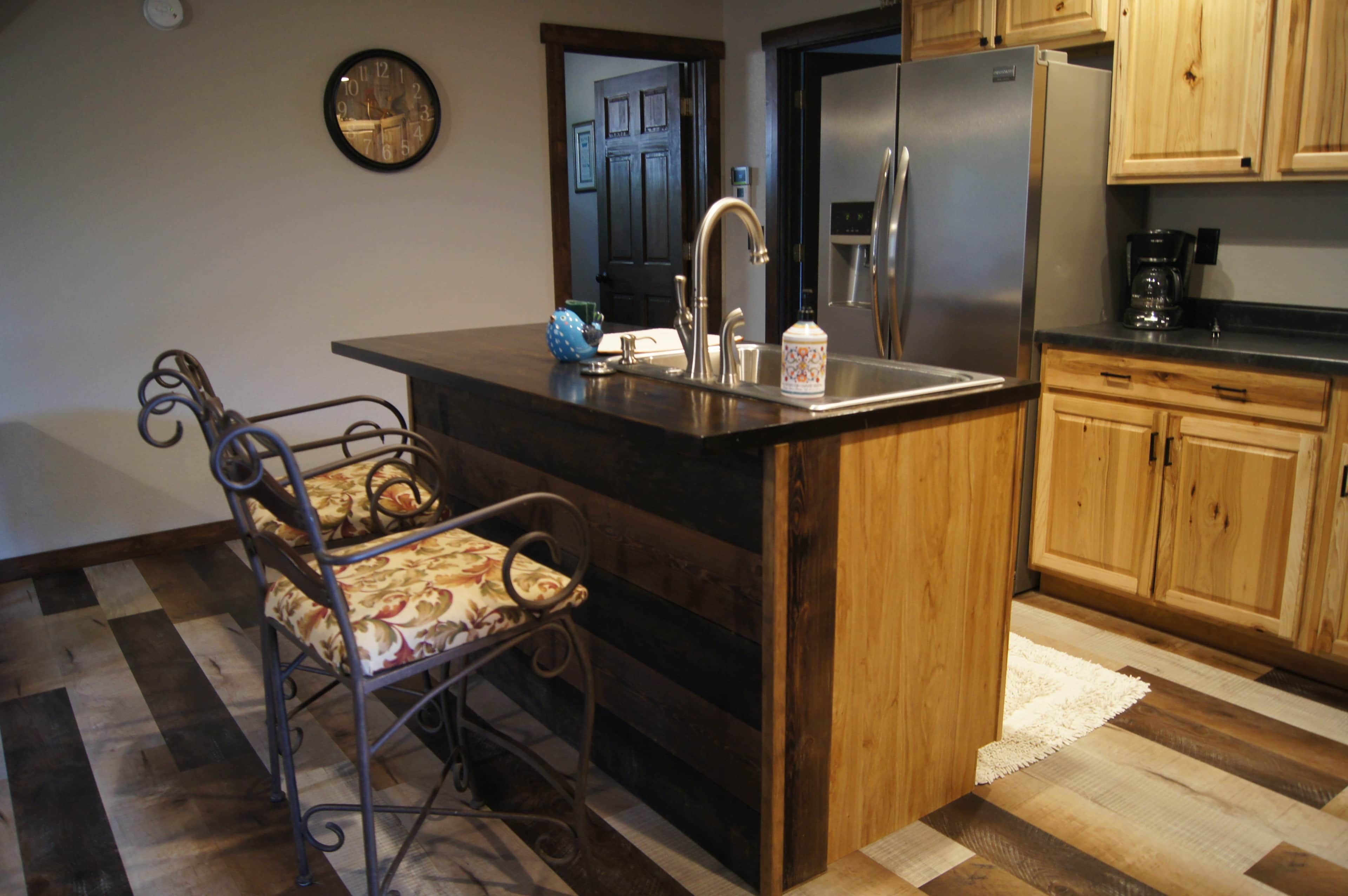 A kitchen with a central island, stainless steel appliances, wooden cabinets, a clock, and a patterned chair.