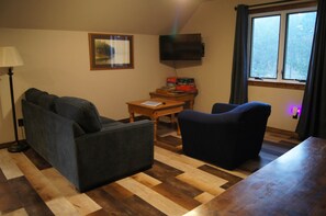A room with a sofa, a chair, a table, a lamp, a TV, and a window. - Elk Haven Vacation Cabins, Custer SD, The Blue Bird's Nest (Custer)