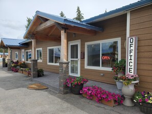 A building with a wooden exterior, a porch with flower planters, and a sign indicating an office.
