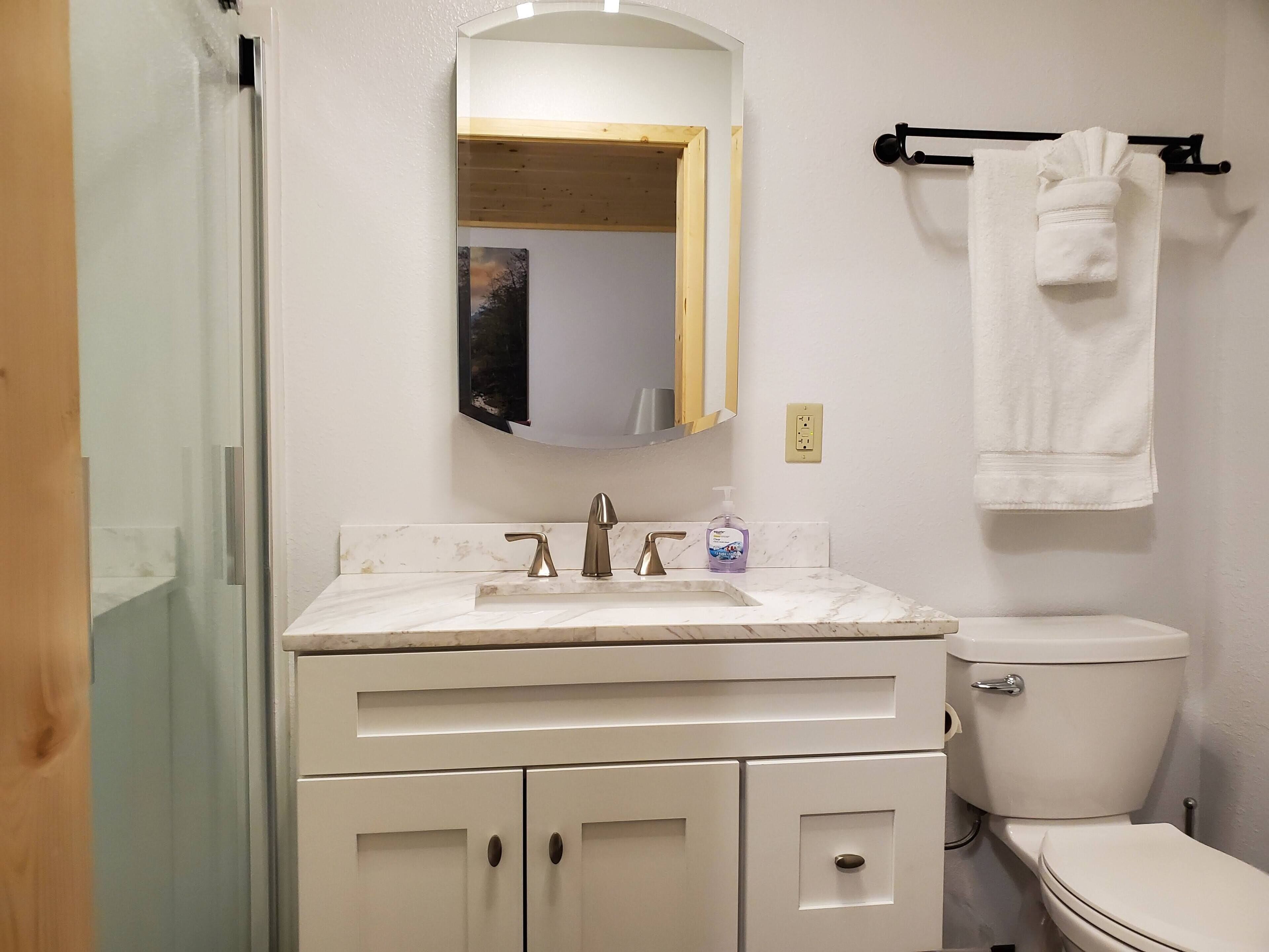 A bathroom with a white sink, two faucets, a mirror, a toilet, and a towel rack.
