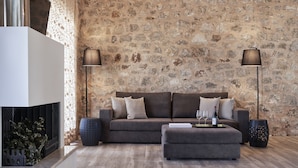 Ein modernes Wohnzimmer mit Steinwand, einer Couch, einem Hocker und zwei Stehlampen.