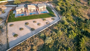 Ein modernes, zweistöckiges Haus mit Swimmingpool, umgeben von einem angelegten Garten und einer bewaldeten Hügelsicht.