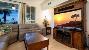 Een woonkamer met een grote flatscreen televisie, een bank, een salontafel en een raam met zonwering.
