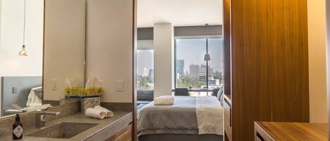 Ein modernes Hotelzimmer mit einem großen Bett, einem Badezimmer mit Granitplatte und Blick auf die Stadt durch große Fenster.