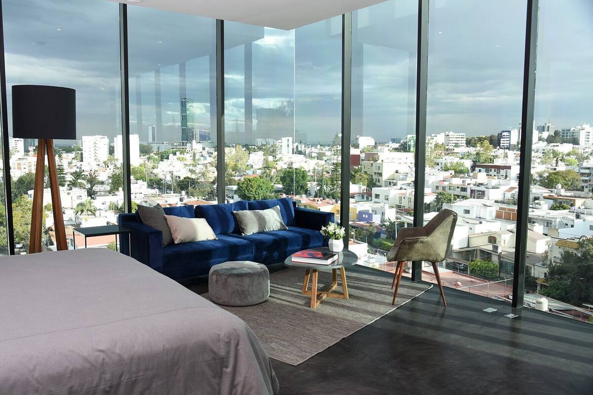 Ein modernes Schlafzimmer mit einem großen Bett, einem blauen Sofa, einem kleinen runden Hocker und einem Sessel.