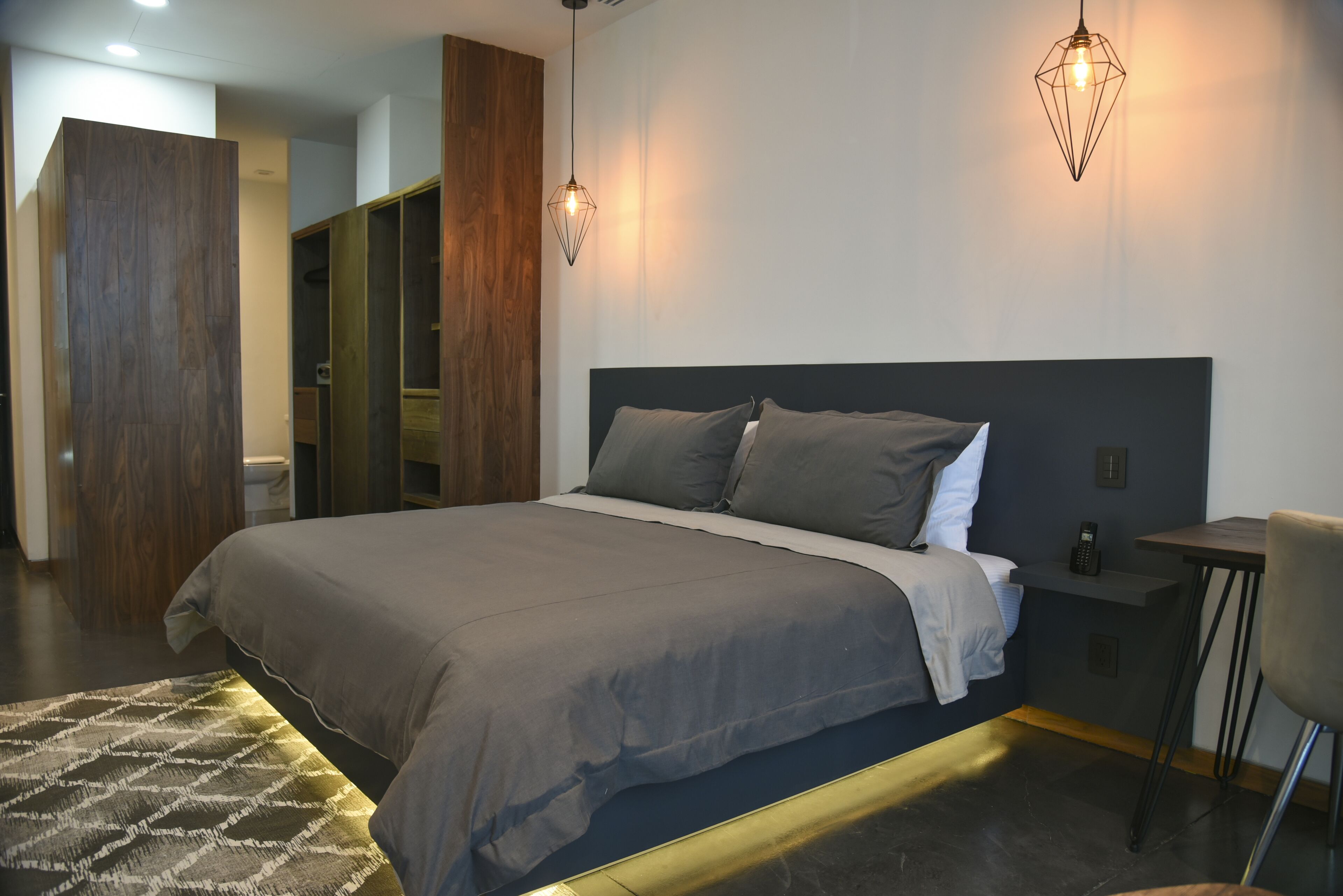 A modern bedroom with a large bed, a bedside table, and a wardrobe.