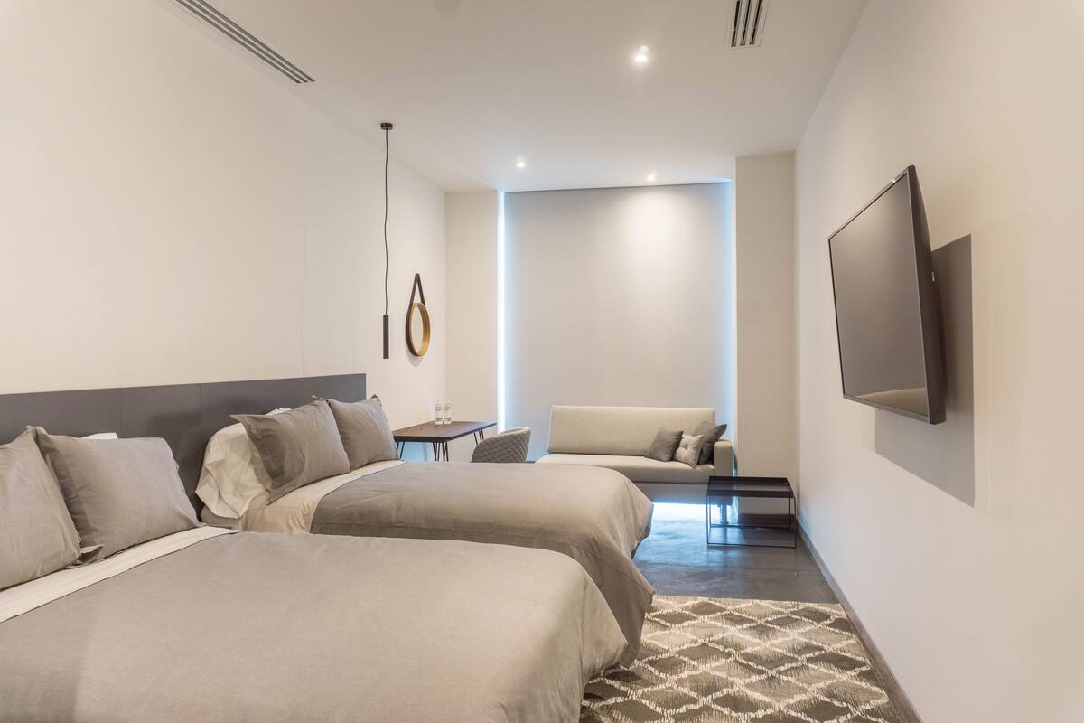 Ein modernes Hotelzimmer mit zwei Betten, einer Sitzecke, einem Fernseher und einem kleinen Tisch.