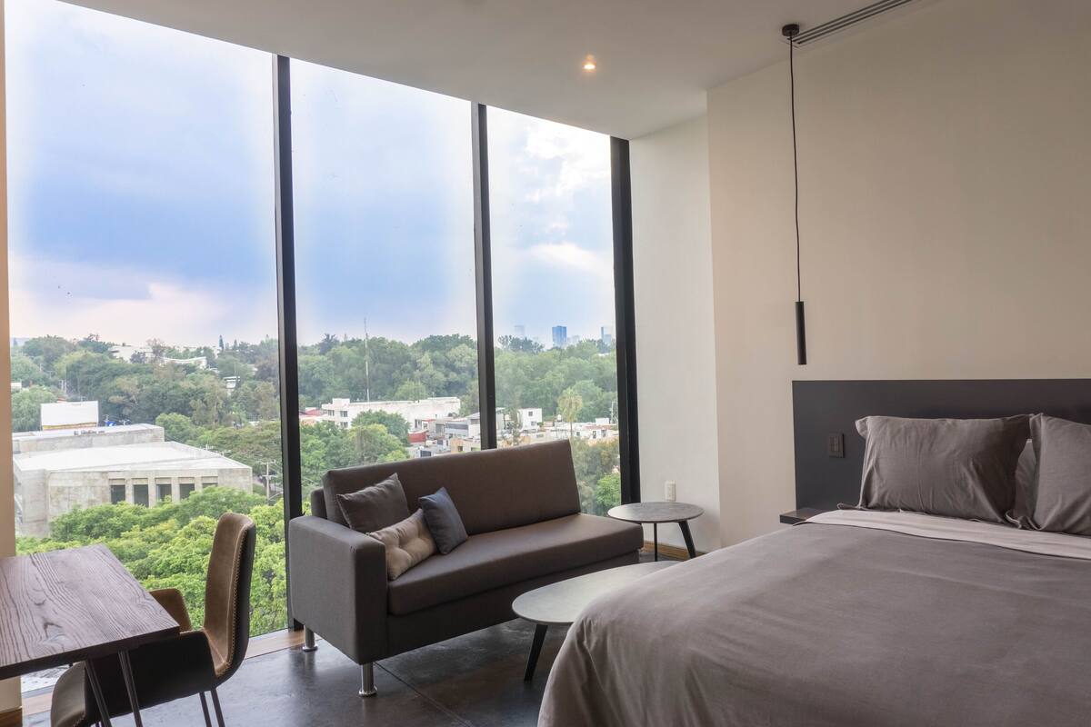 Ein modernes Hotelzimmer mit großem Fenster, einer Couch, einem kleinen Tisch und einem Bett.