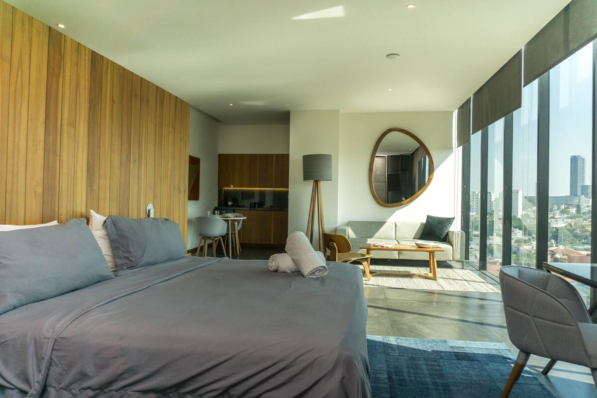 Ein modernes Hotelzimmer mit einem großen Bett, einer Sitzecke mit Blick, einer Küche und einem großen Fenster.