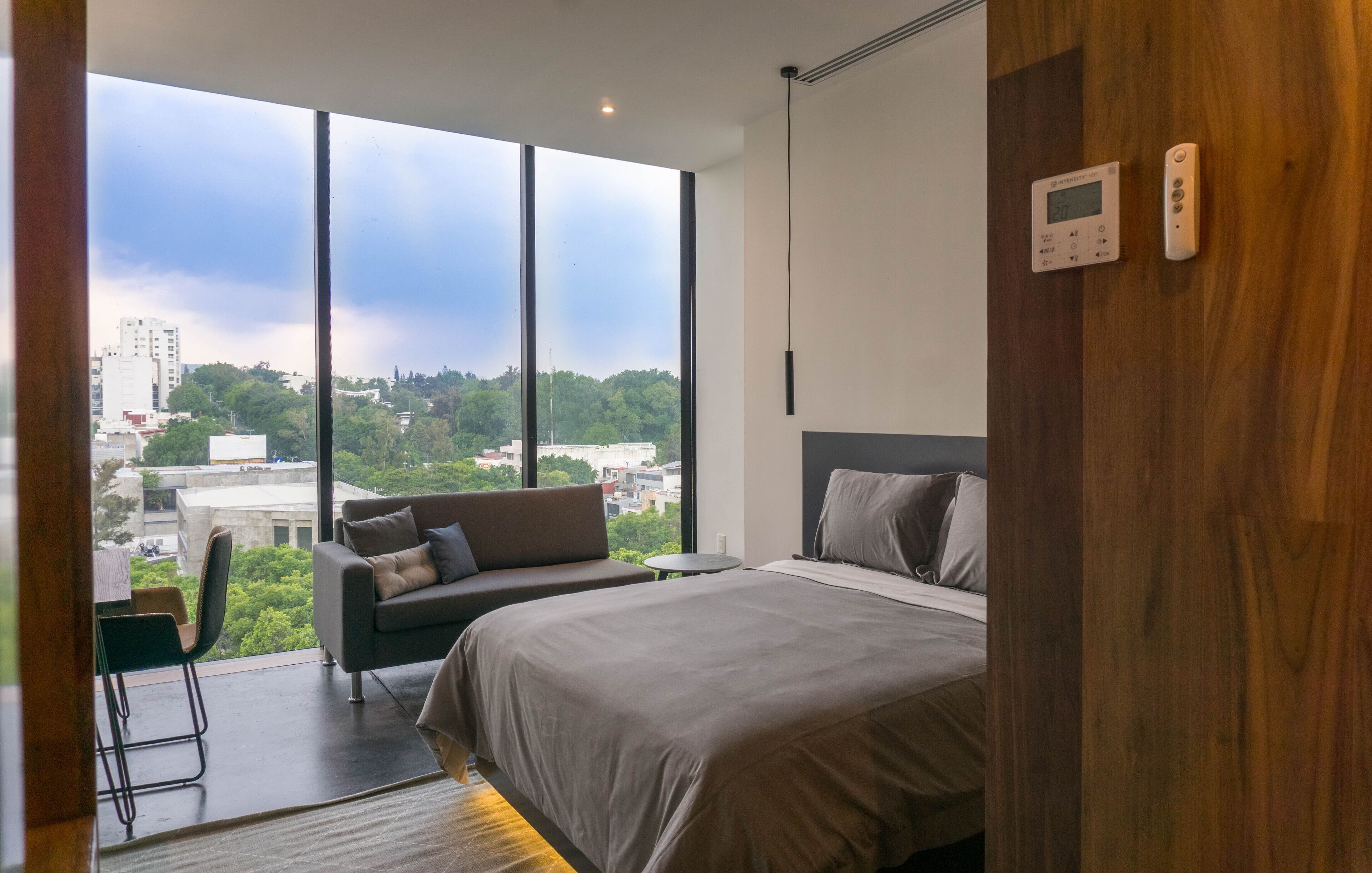 A modern bedroom with a large window, a bed, a sofa, and a small table.