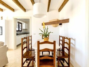 Een eetgedeelte met een houten tafel en stoelen, een potplant en een keuken op de achtergrond.