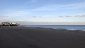 A beach with a clear sky, a sandy shore, and buildings in the background.