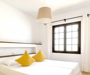 Een hotelkamer met een bed, een raam met gordijnen en een hanglamp.