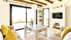 A modern living room with a glass coffee table, sofas, a TV, and a balcony with plants.