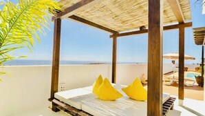 A balcony with a wooden pergola, a white sofa with yellow cushions, and a view of the sea.
