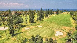 Un parcours de golf offrant une vue dégagée sur l’océan, entouré de palmiers et de quelques bâtiments.