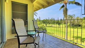 Un balcon avec deux chaises et une table, donnant sur une pelouse bien entretenue et des palmiers.