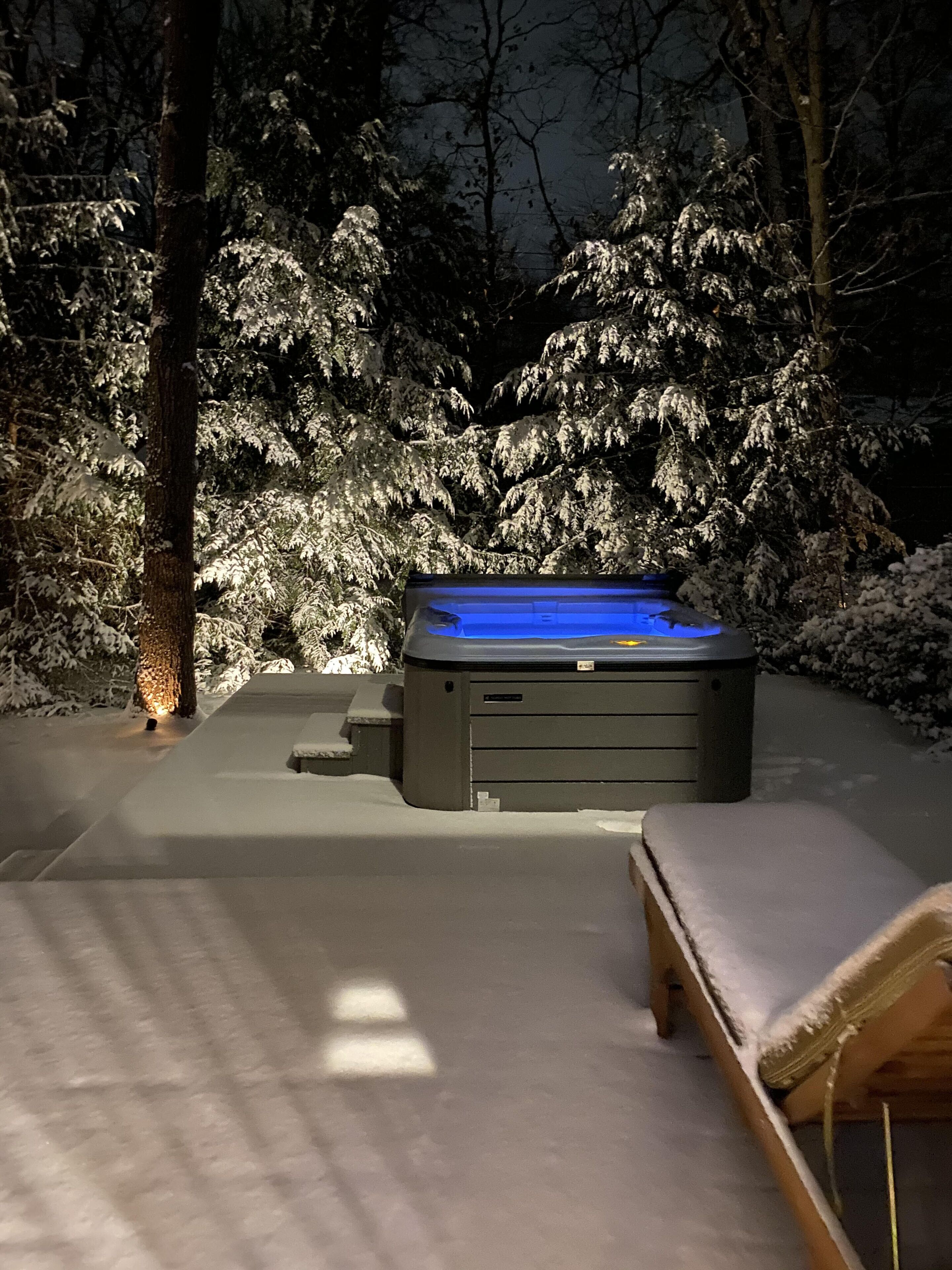 Ein Whirlpool in einer verschneiten Außenanlage mit einer Bank in der Nähe.