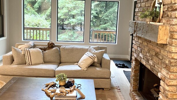 A cozy living room with a large window, a fireplace, and a comfortable sofa.