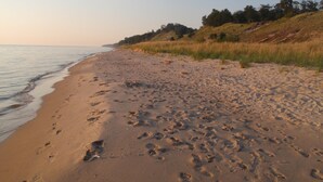 A sandy beach with footprints and a grassy hill in the background.