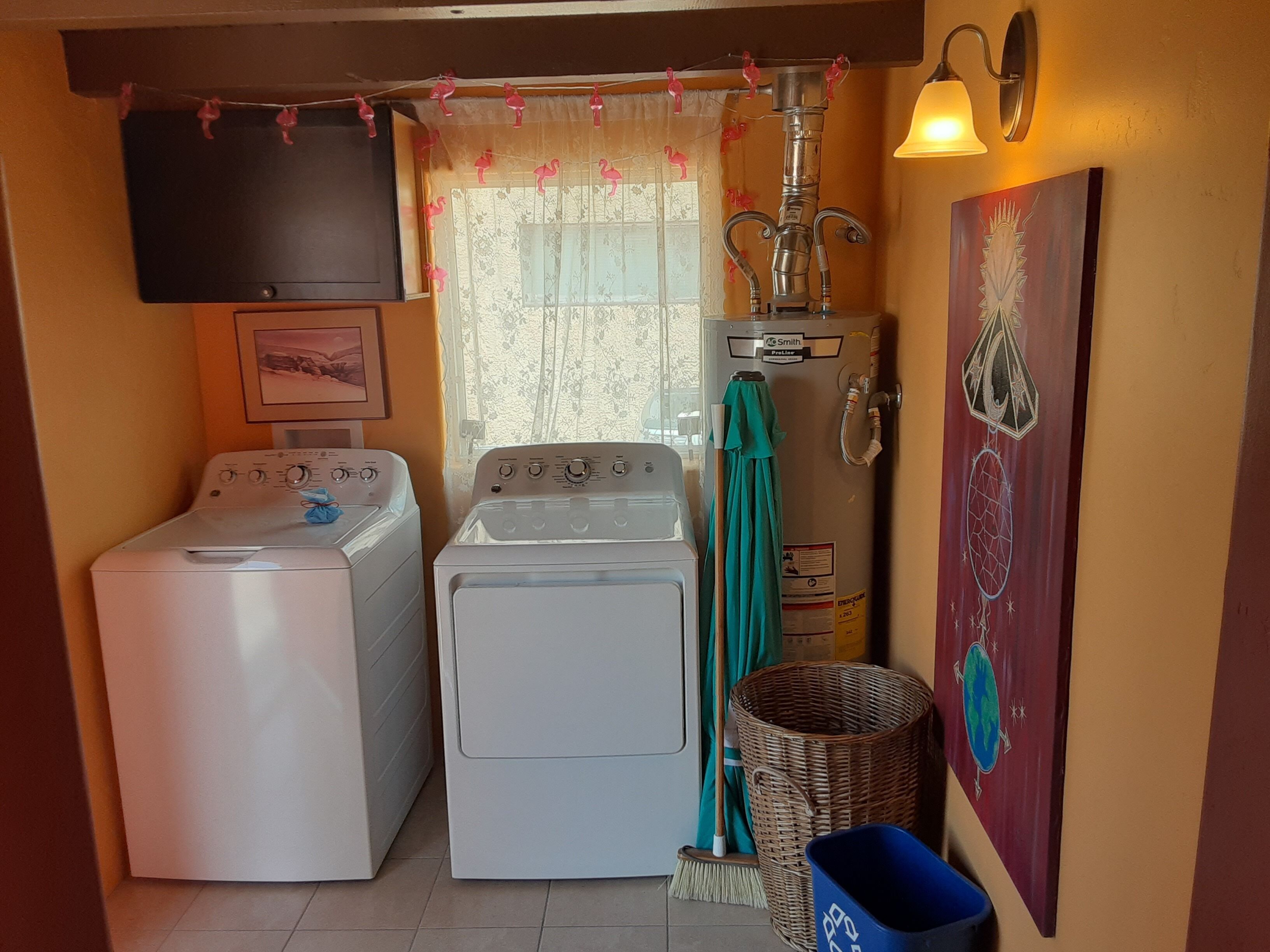 A laundry room with two washing machines, a drying rack, a broom, and a wall-mounted sink.