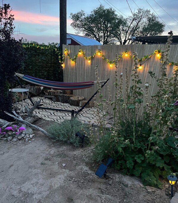 A hammock, a patterned outdoor rug, and a wooden fence with string lights.