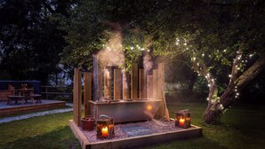 Un jacuzzi en una estructura de madera rodeado de árboles, con un banco y faroles.
