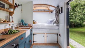 Una habitación pequeña y luminosa, con cama, lavamanos y una kitchenette.